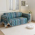 Bohemian-style sofa cover featuring vibrant blue, teal, and navy geometric tribal patterns with white tassel edging.