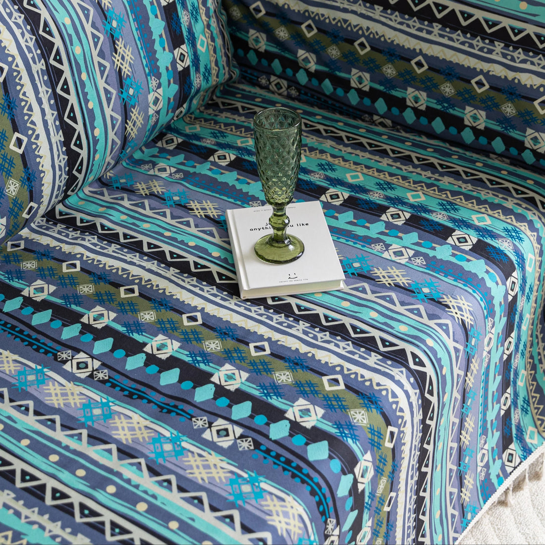 Vibrant sofa cover with blue, teal, and navy geometric tribal patterns, accented with white tassel trim, creating a bold and stylish statement for modern or bohemian living room décor.