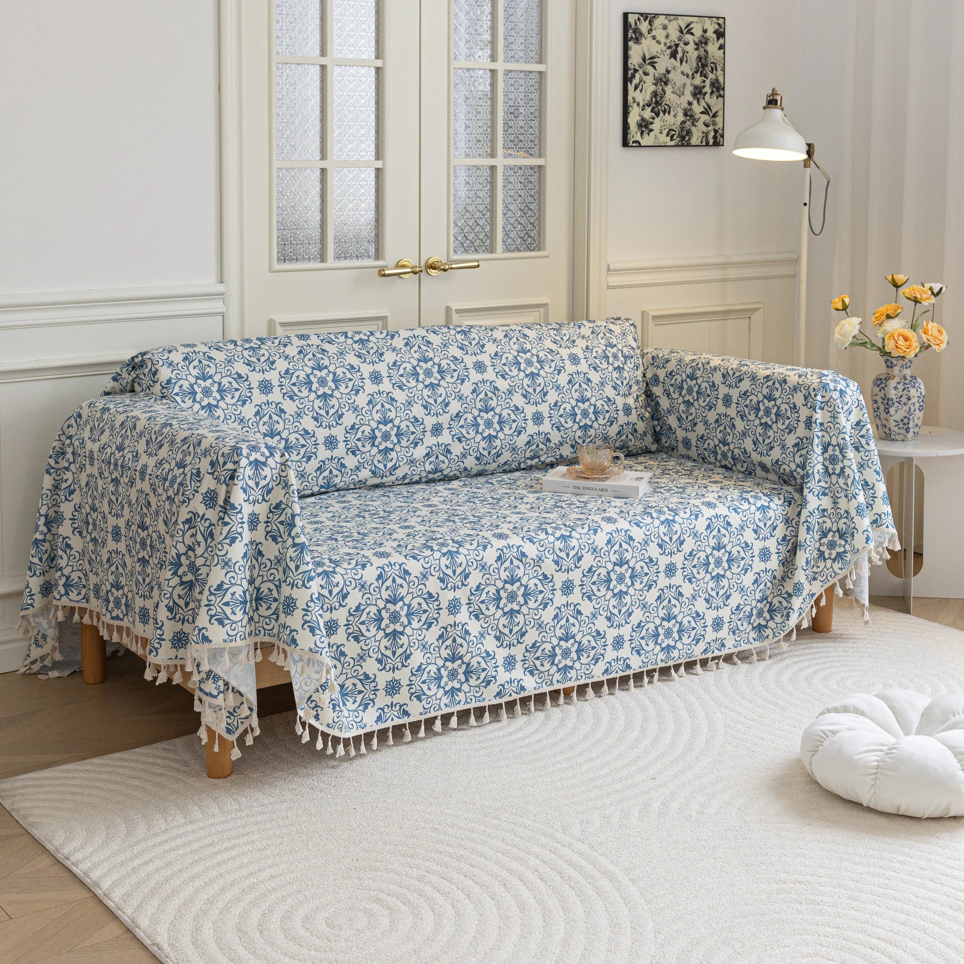 Elegant sofa cover with a blue floral damask pattern on a white background, finished with decorative white tassel fringe,