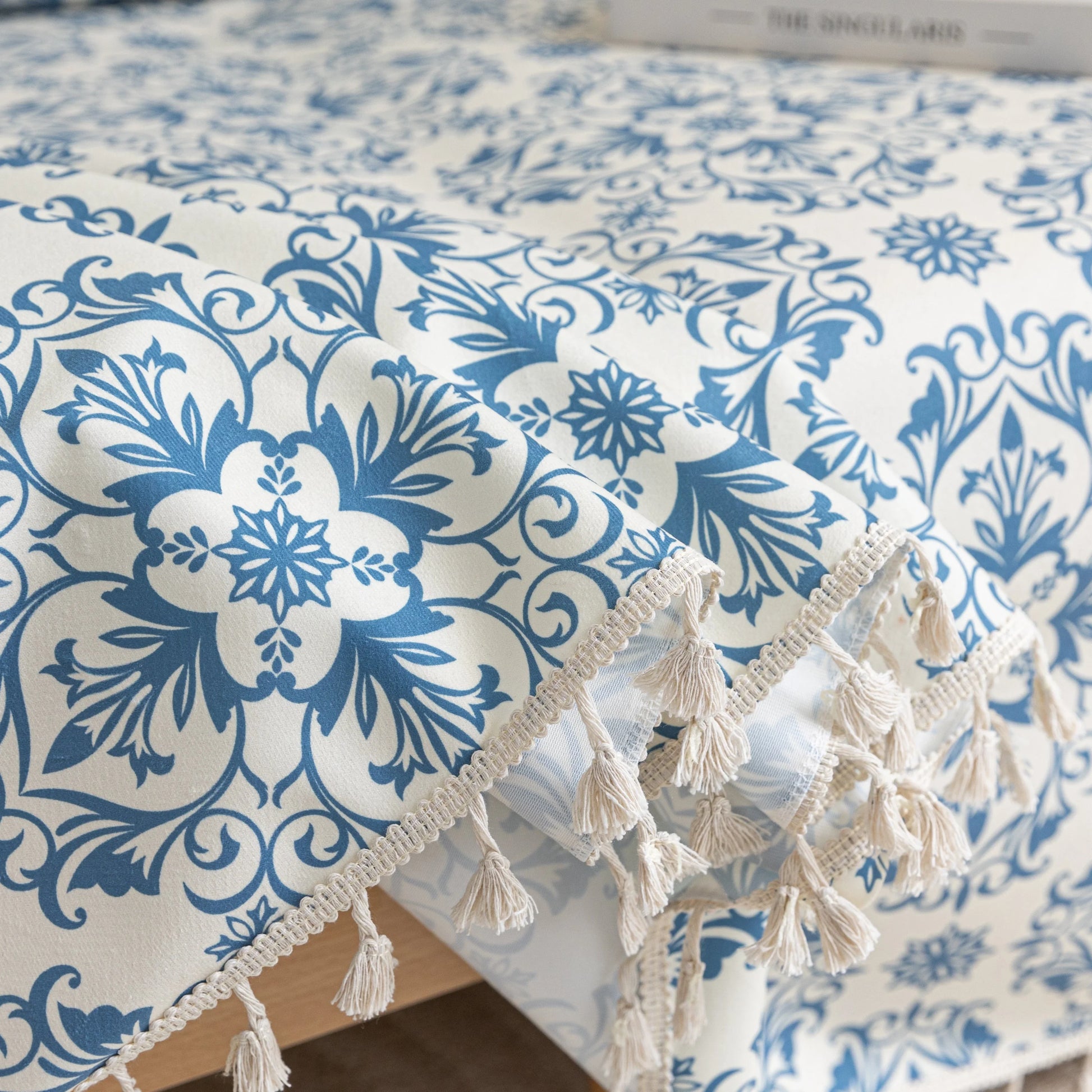 Elegant sofa cover with a blue floral damask pattern on a white background, finished with decorative white tassel fringe,