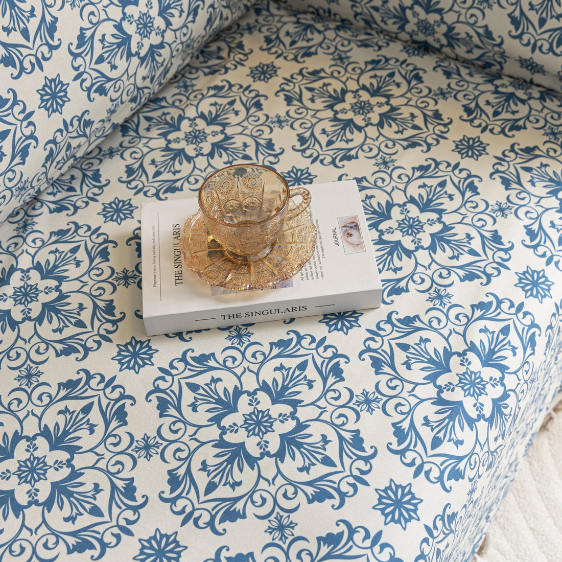 Elegant sofa cover with a blue floral damask pattern on a white background, finished with decorative white tassel fringe,