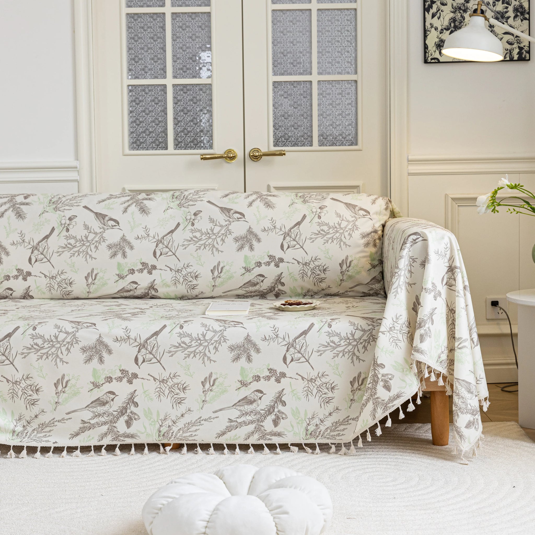 Beige sofa cover with delicate botanical and bird illustrations in brown and light green, featuring nature-inspired patterns