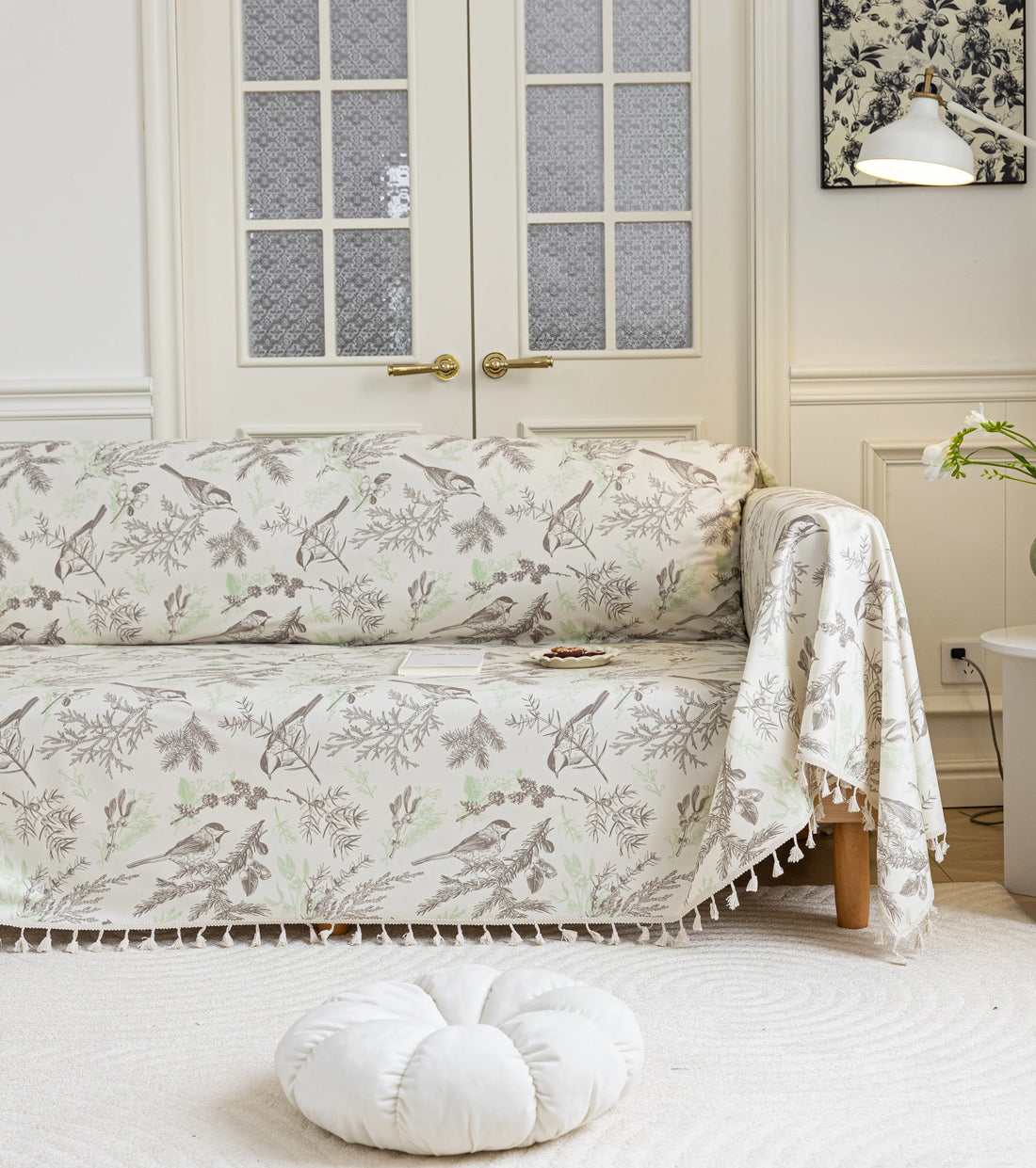 Beige sofa cover with delicate botanical and bird illustrations in brown and light green, featuring nature-inspired patterns
