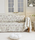 Beige sofa cover with delicate botanical and bird illustrations in brown and light green, featuring nature-inspired patterns