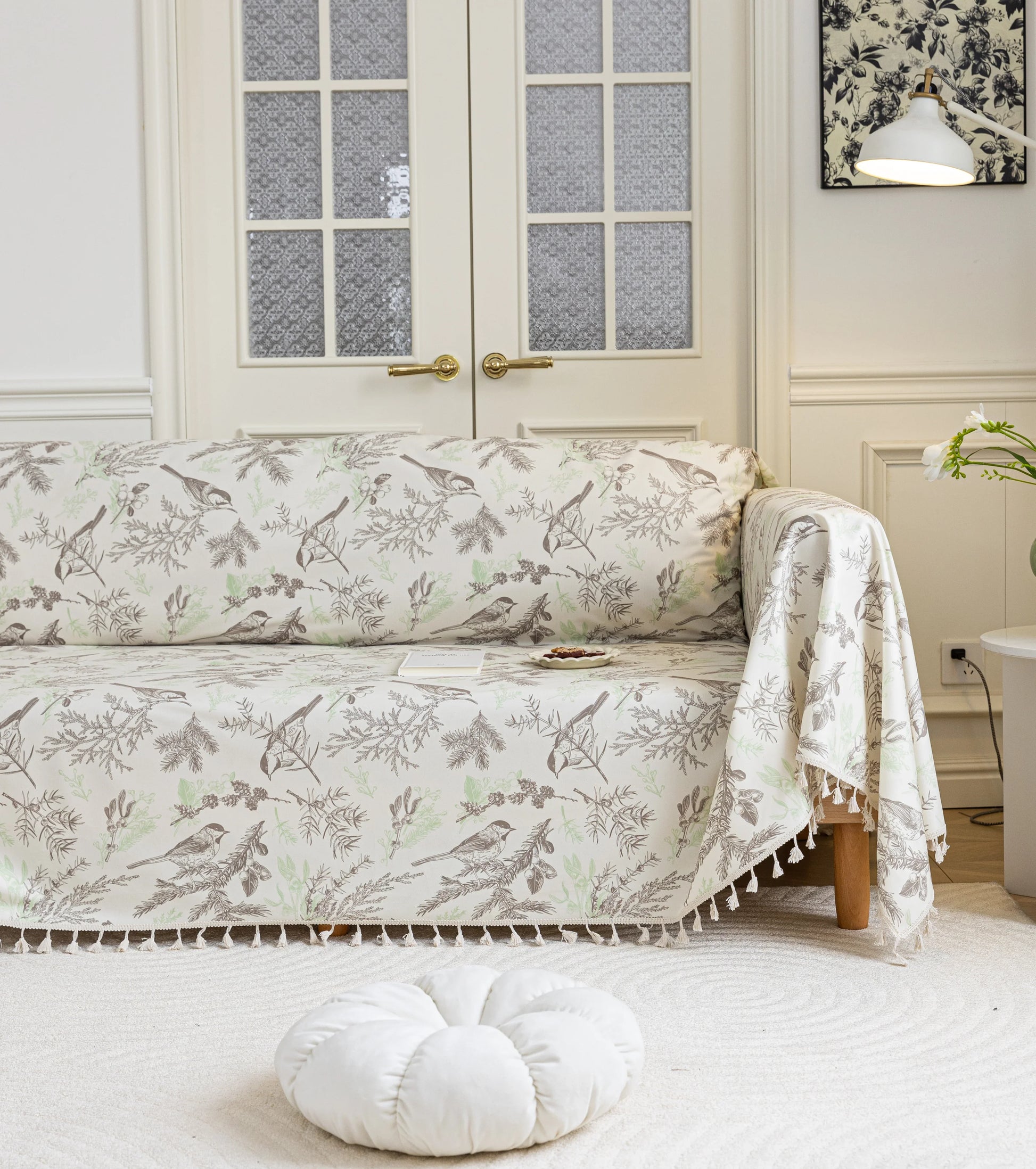 Beige sofa cover with delicate botanical and bird illustrations in brown and light green, featuring nature-inspired patterns
