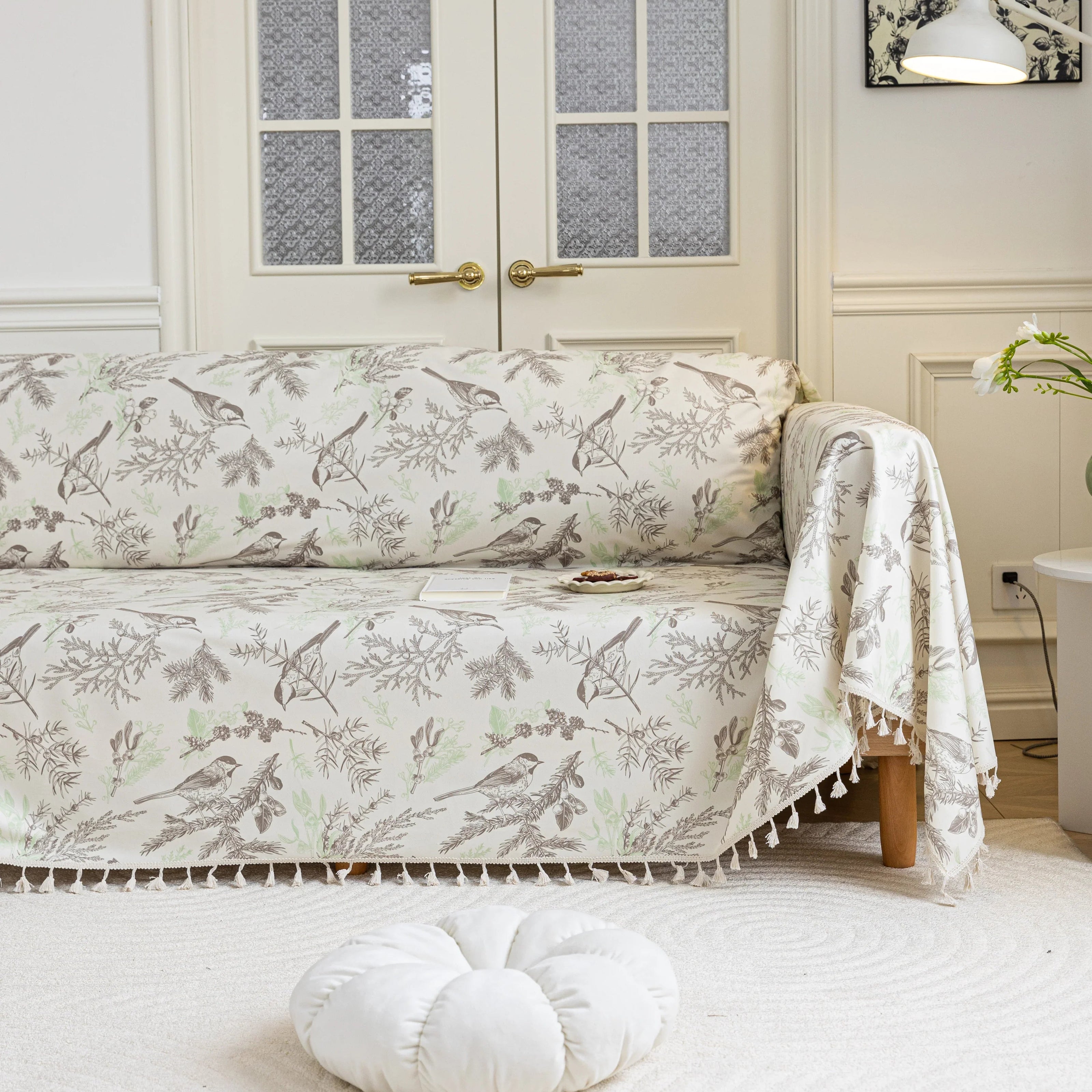 Beige sofa cover with delicate botanical and bird illustrations in brown and light green, featuring nature-inspired patterns