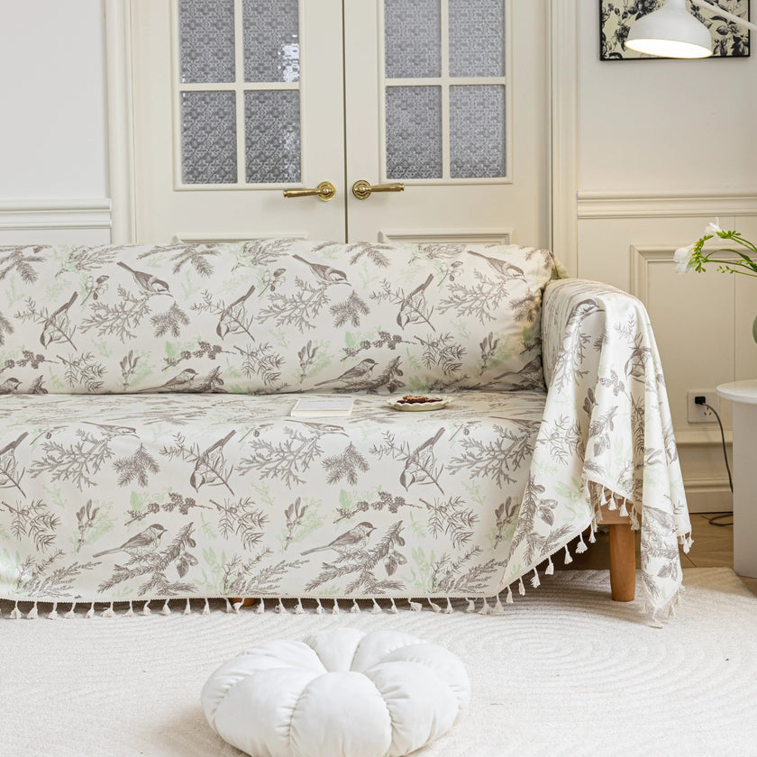 Beige sofa cover with delicate botanical and bird illustrations in brown and light green, featuring nature-inspired patterns