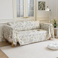 Beige sofa cover with delicate botanical and bird illustrations in brown and light green, featuring nature-inspired patterns