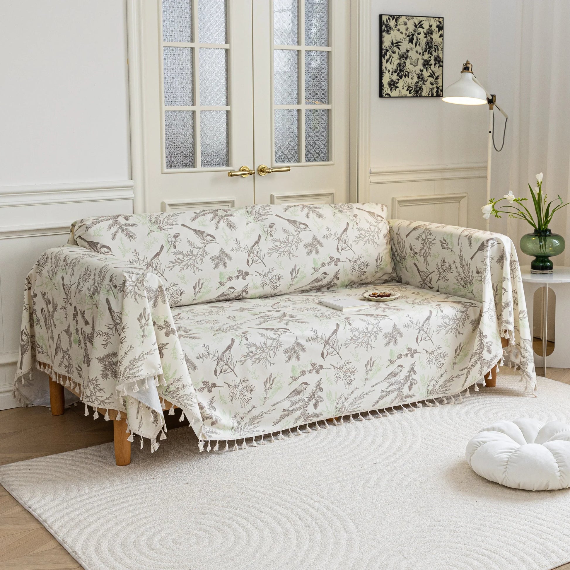 Beige sofa cover with delicate botanical and bird illustrations in brown and light green, featuring nature-inspired patterns