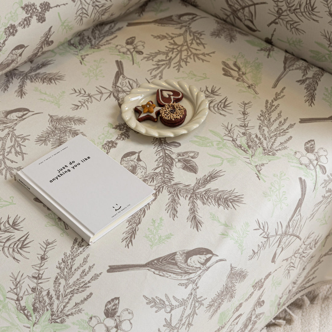Beige sofa cover with delicate botanical and bird illustrations in brown and light green, featuring nature-inspired patterns