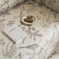 Beige sofa cover with delicate botanical and bird illustrations in brown and light green, featuring nature-inspired patterns