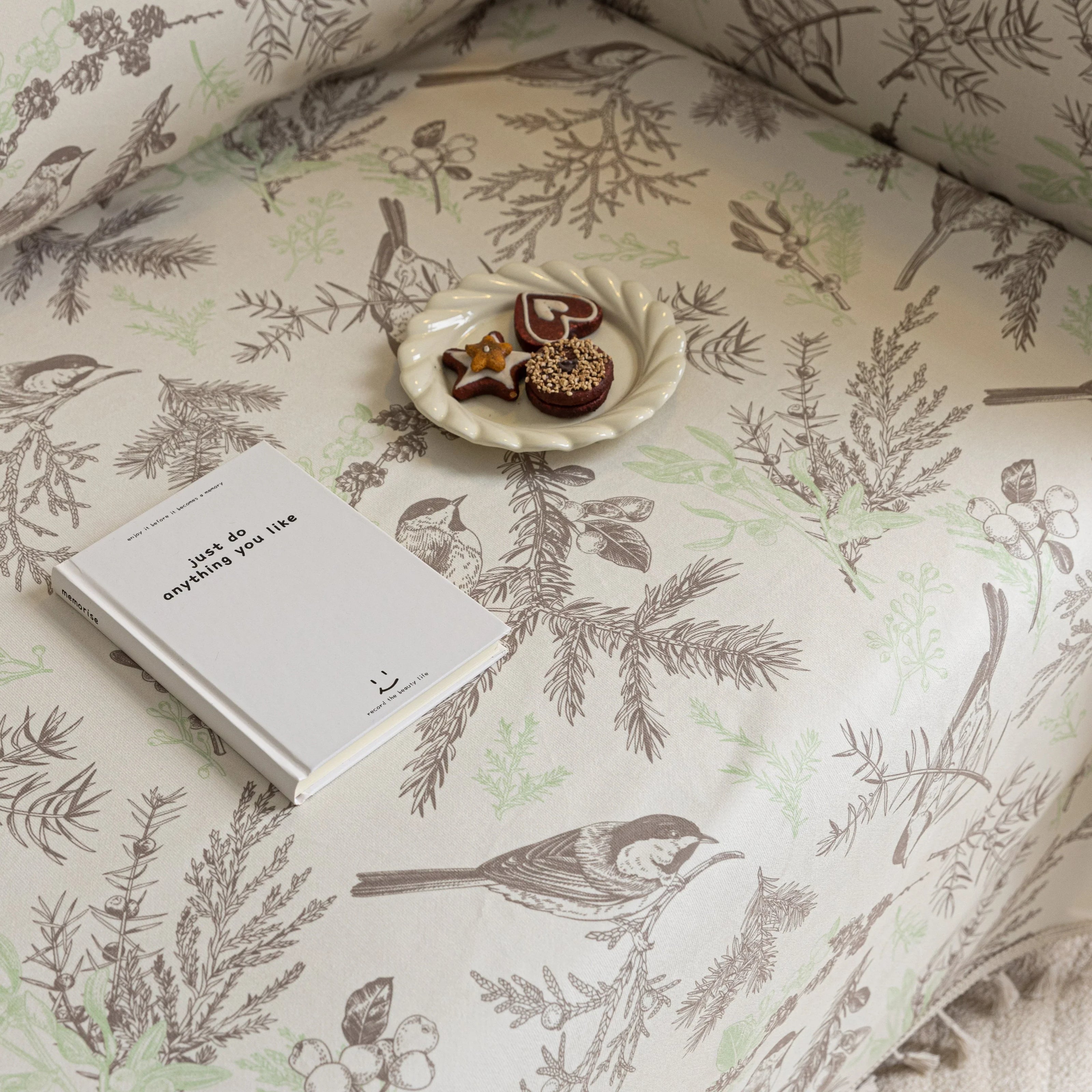 Beige sofa cover with delicate botanical and bird illustrations in brown and light green, featuring nature-inspired patterns
