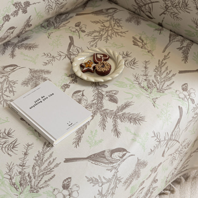 Beige sofa cover with delicate botanical and bird illustrations in brown and light green, featuring nature-inspired patterns