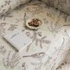 Beige sofa cover with delicate botanical and bird illustrations in brown and light green, featuring nature-inspired patterns