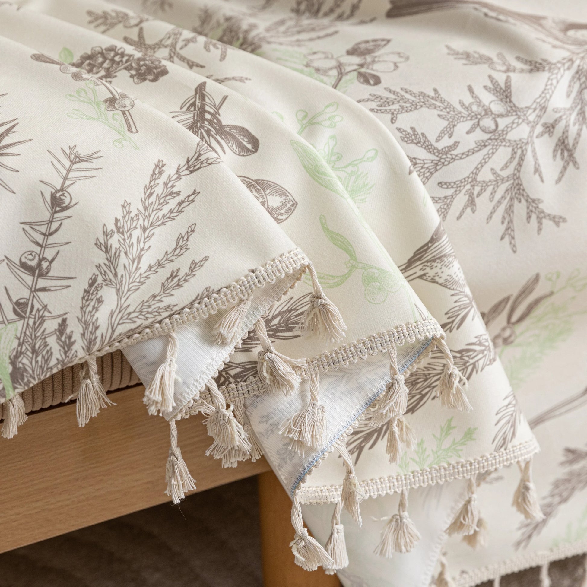 Beige sofa cover with delicate botanical and bird illustrations in brown and light green, featuring nature-inspired patterns.