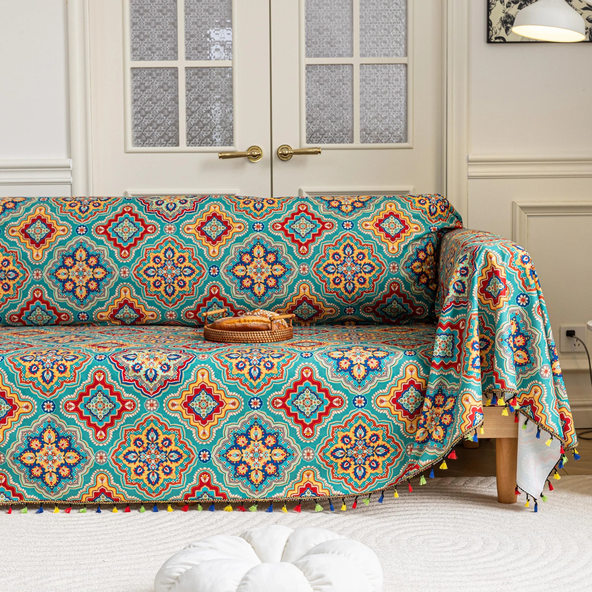 Colorful sofa cover with vibrant Moroccan-style geometric patterns in teal, red, yellow, and blue, finished with multicolor tassel trim.