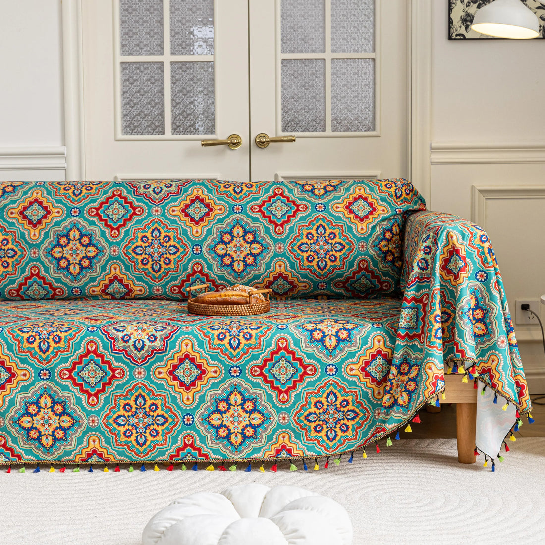 Colorful sofa cover with vibrant Moroccan-style geometric patterns in teal, red, yellow, and blue, finished with multicolor tassel trim.