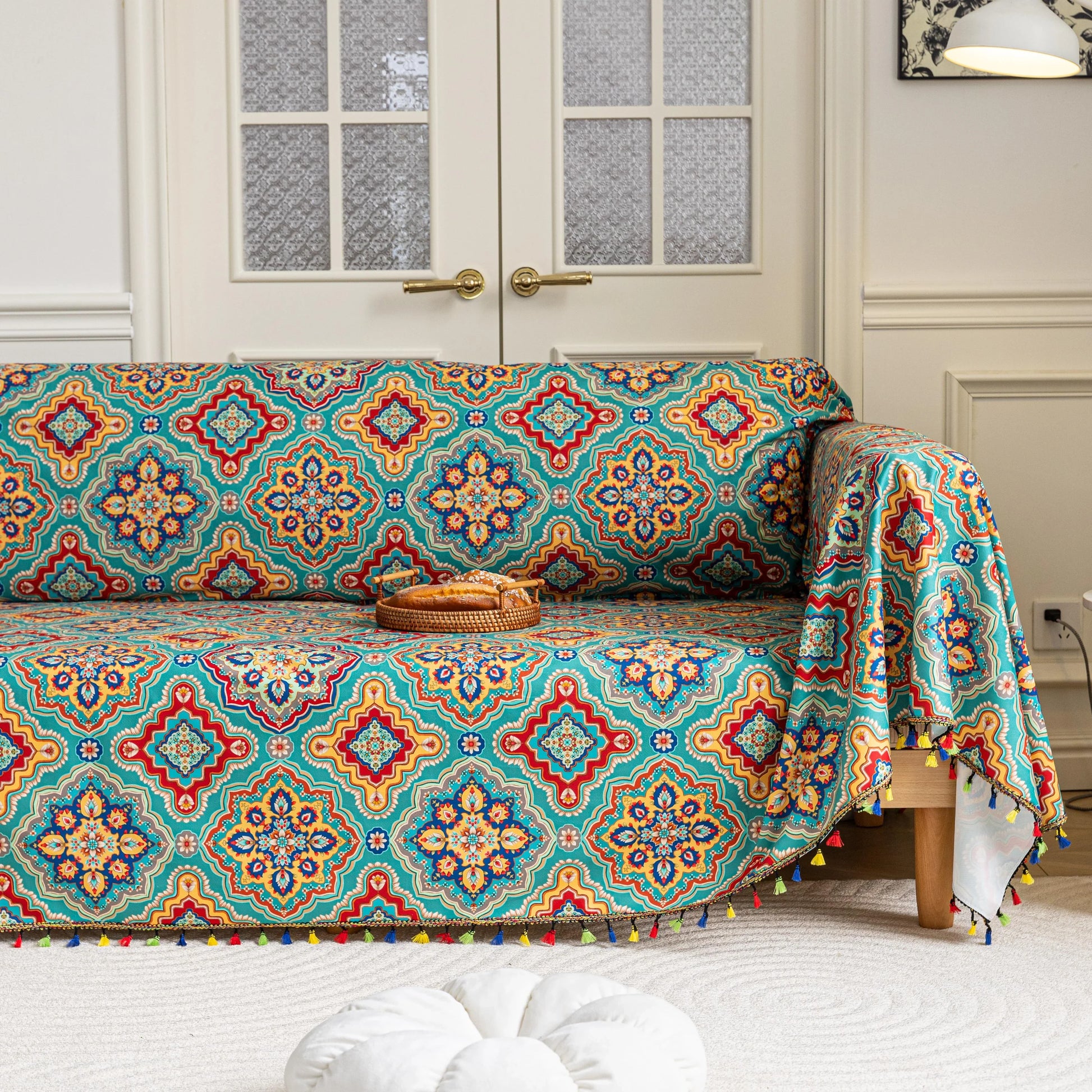 Colorful sofa cover with vibrant Moroccan-style geometric patterns in teal, red, yellow, and blue, finished with multicolor tassel trim.