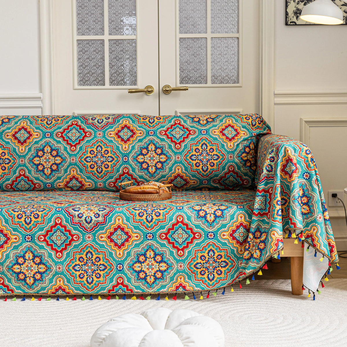 Colorful sofa cover with vibrant Moroccan-style geometric patterns in teal, red, yellow, and blue, finished with multicolor tassel trim.