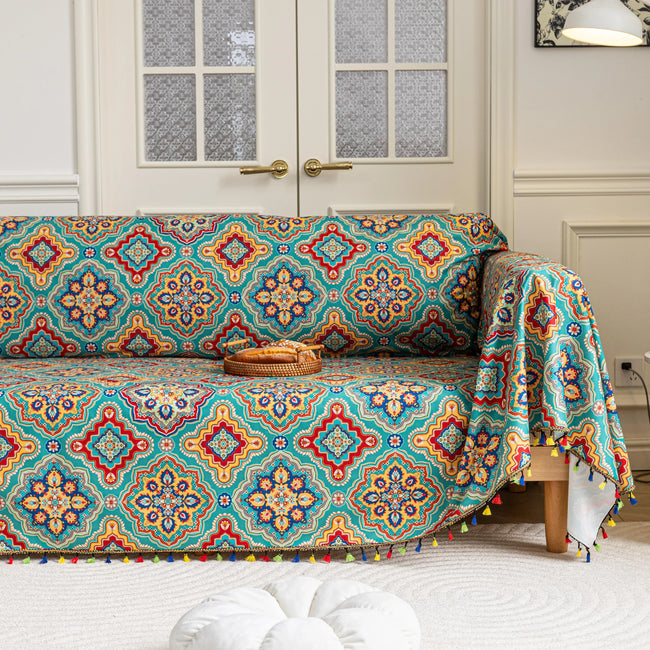 Colorful sofa cover with vibrant Moroccan-style geometric patterns in teal, red, yellow, and blue, finished with multicolor tassel trim.