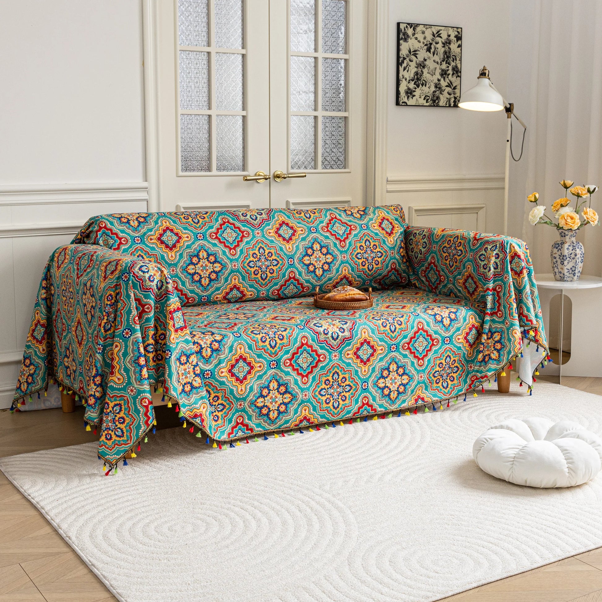 Colorful sofa cover with vibrant Moroccan-style geometric patterns in teal, red, yellow, and blue, finished with multicolor tassel trim.
