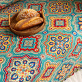 Colorful sofa cover with vibrant Moroccan-style geometric patterns in teal, red, yellow, and blue, finished with multicolor tassel trim.