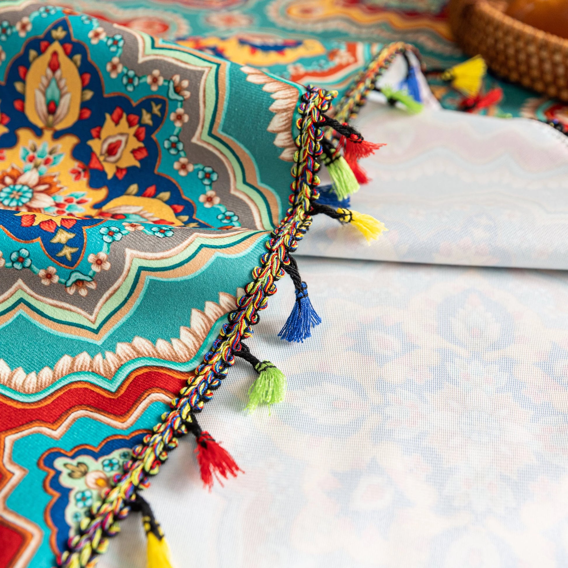 Colorful sofa cover with vibrant Moroccan-style geometric patterns in teal, red, yellow, and blue, finished with multicolor tassel trim.