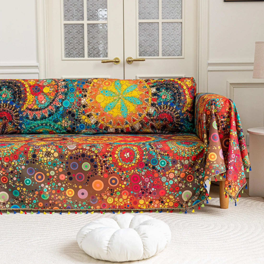 Colorful sofa cover with abstract circular and mandala-inspired patterns in vibrant shades of yellow, red, turquoise, and orange on a dark background, accented with multicolor tassel trim.