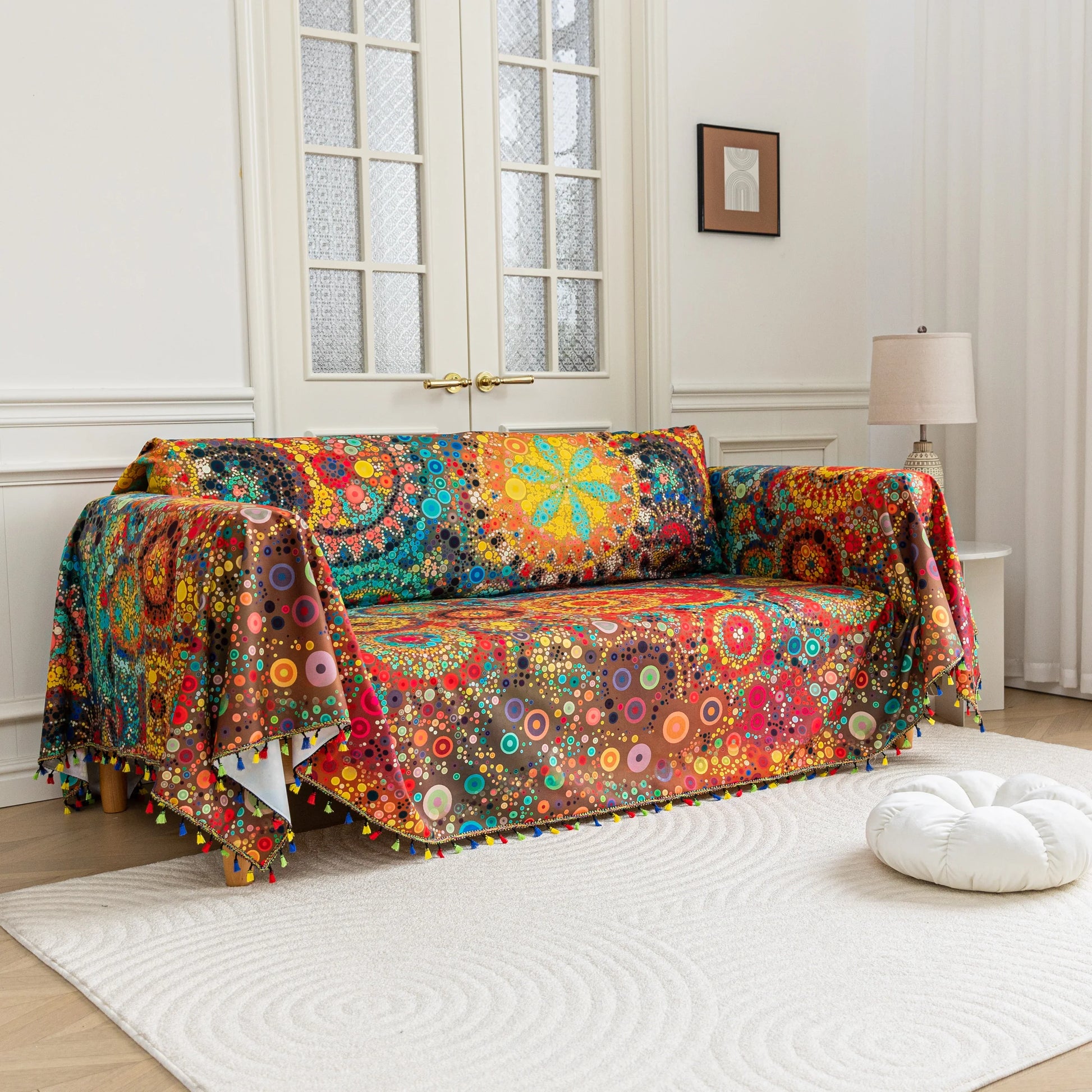 Colorful sofa cover with abstract circular and mandala-inspired patterns in vibrant shades of yellow, red, turquoise, and orange on a dark background, accented with multicolor tassel trim.