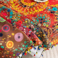 Colorful sofa cover with abstract circular and mandala-inspired patterns in vibrant shades of yellow, red, turquoise, and orange on a dark background, accented with multicolor tassel trim.