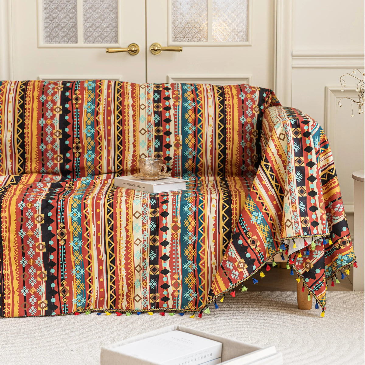 Southwestern-inspired sofa cover with vibrant tribal geometric patterns in red, orange, black, and turquoise, accented with colorful tassels.