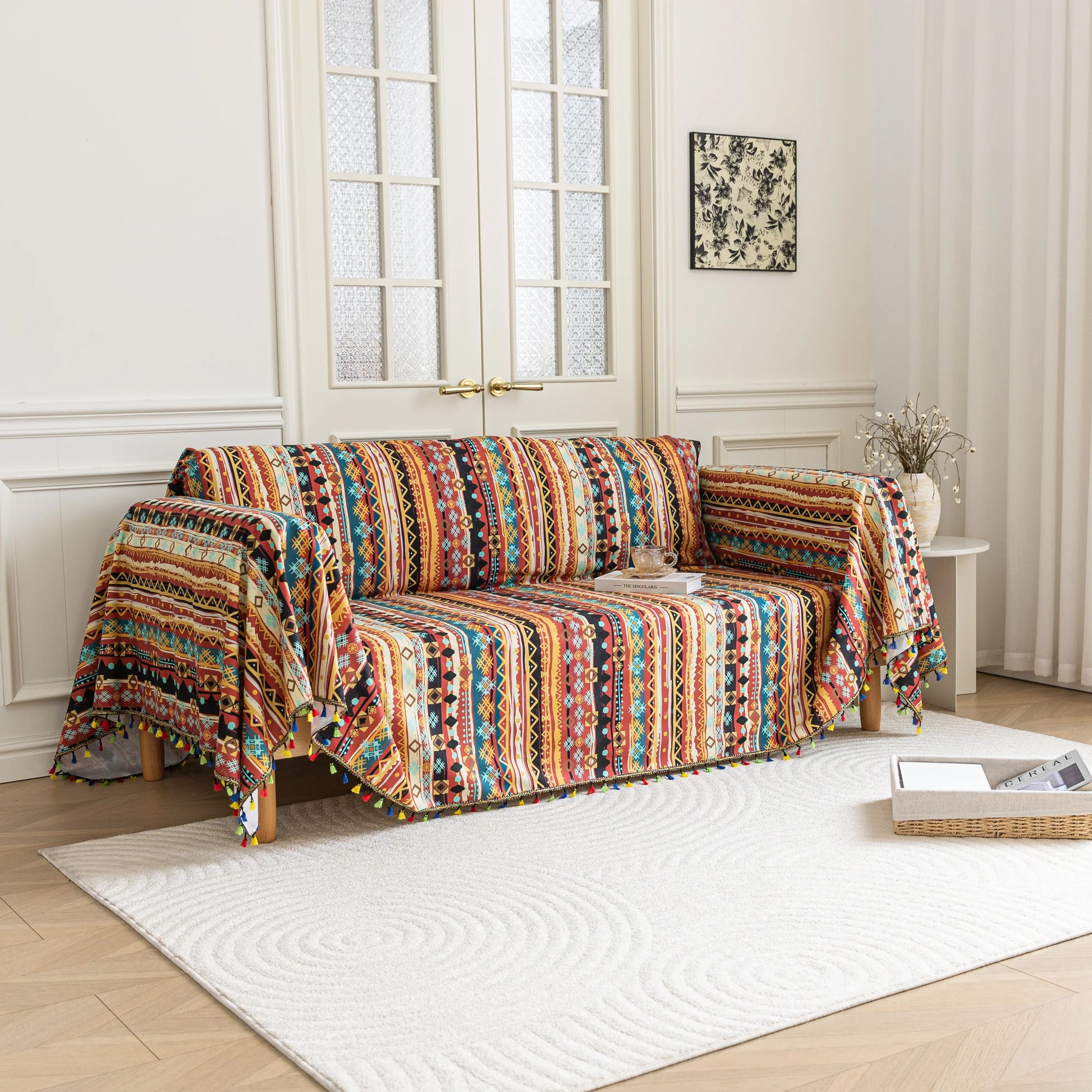 Southwestern-inspired sofa cover with vibrant tribal geometric patterns in red, orange, black, and turquoise, accented with colorful tassels.