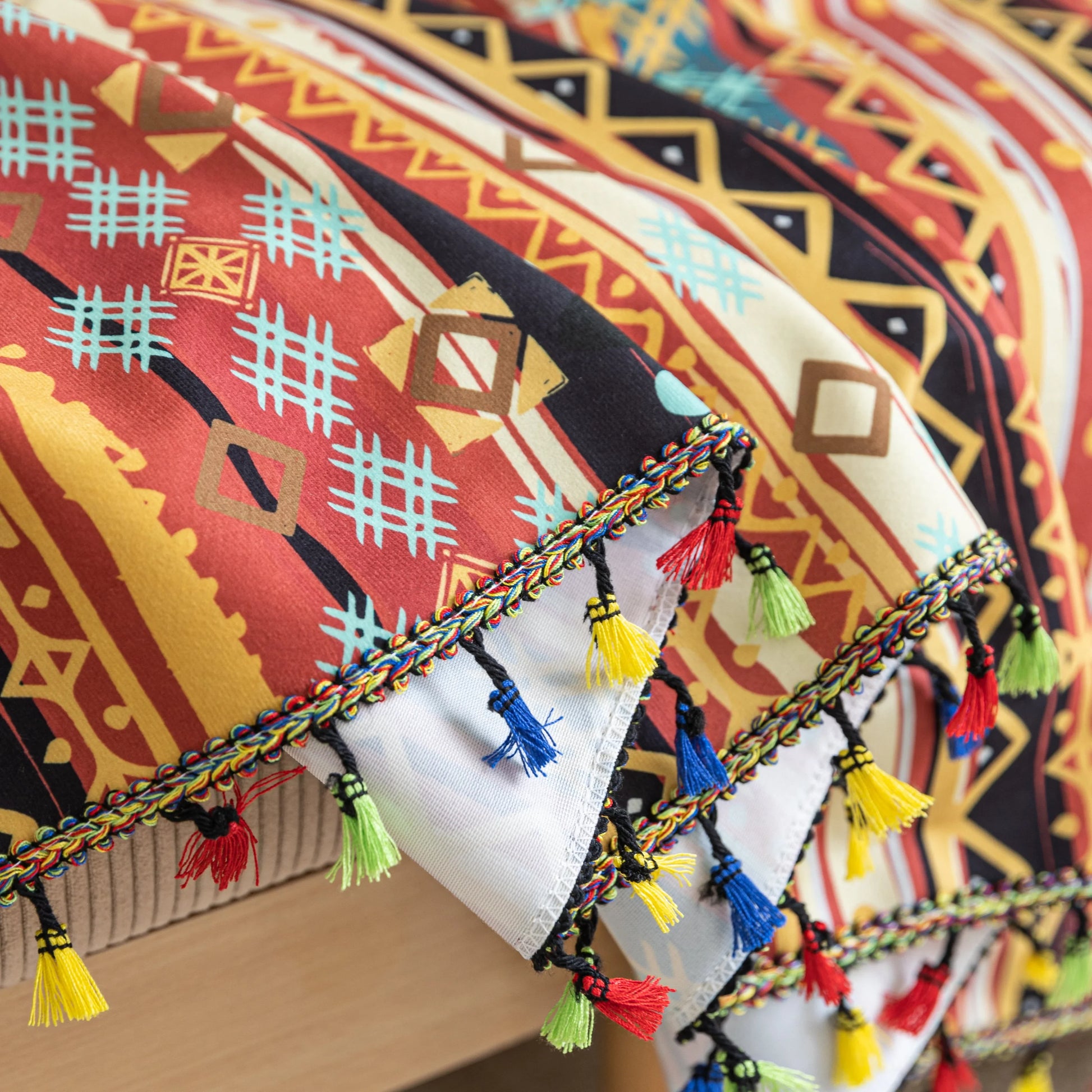 Southwestern-inspired sofa cover with vibrant tribal geometric patterns in red, orange, black, and turquoise, accented with colorful tassels.