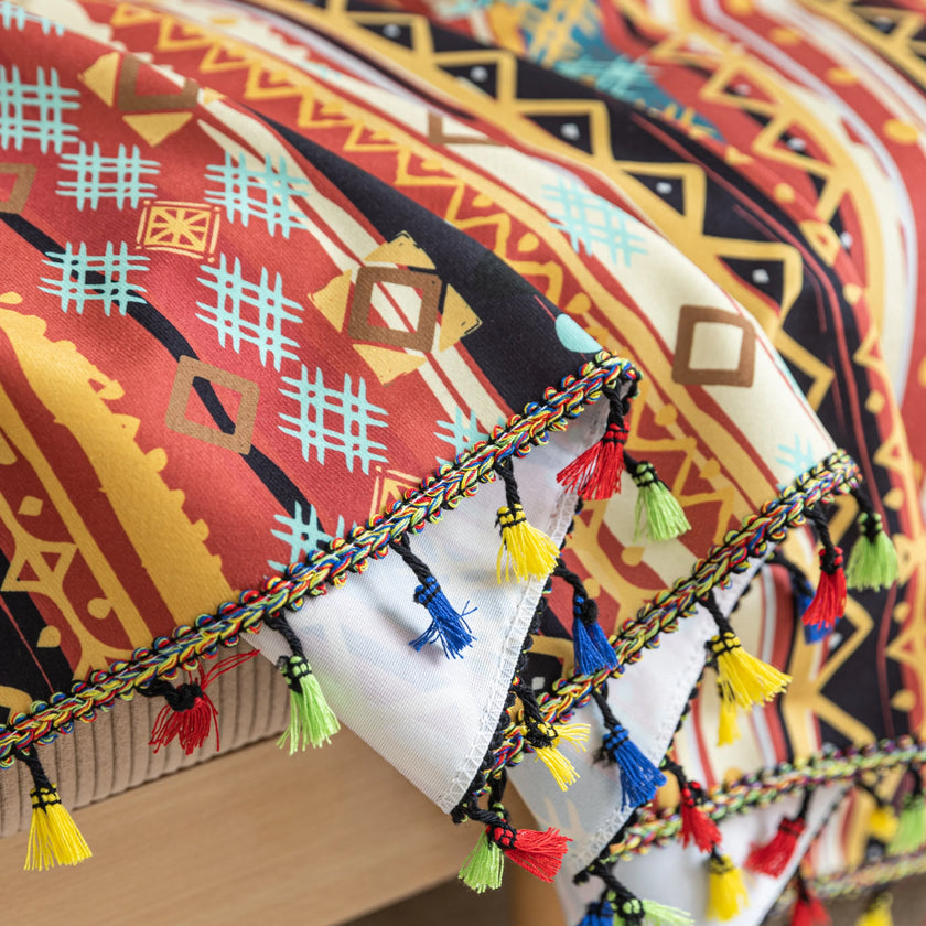 Southwestern-inspired sofa cover with vibrant tribal geometric patterns in red, orange, black, and turquoise, accented with colorful tassels.