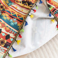 Southwestern-inspired sofa cover with vibrant tribal geometric patterns in red, orange, black, and turquoise, accented with colorful tassels.