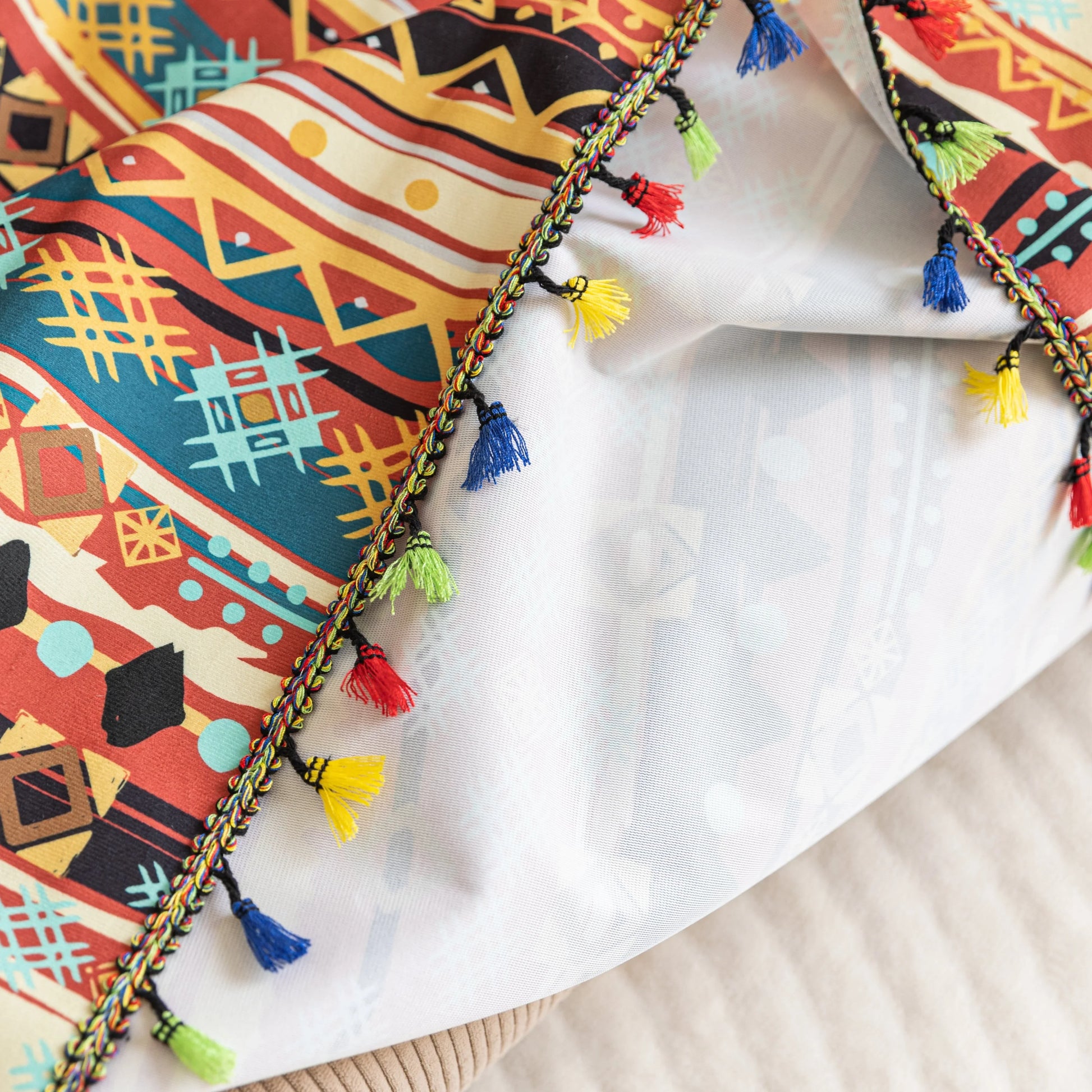 Southwestern-inspired sofa cover with vibrant tribal geometric patterns in red, orange, black, and turquoise, accented with colorful tassels.