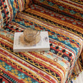 Southwestern-inspired sofa cover with vibrant tribal geometric patterns in red, orange, black, and turquoise, accented with colorful tassels.