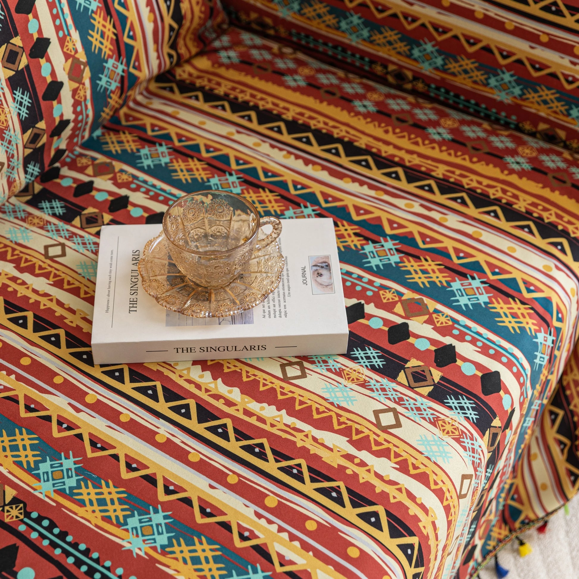 Southwestern-inspired sofa cover with vibrant tribal geometric patterns in red, orange, black, and turquoise, accented with colorful tassels.