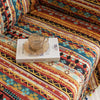 Southwestern-inspired sofa cover with vibrant tribal geometric patterns in red, orange, black, and turquoise, accented with colorful tassels.