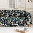 Elegant floral sofa cover with a dark navy background, featuring vibrant blossoms and green foliage, accented with white tassel trim.