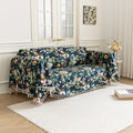 Elegant floral sofa cover with a dark navy background, featuring vibrant blossoms and green foliage, accented with white tassel trim.
