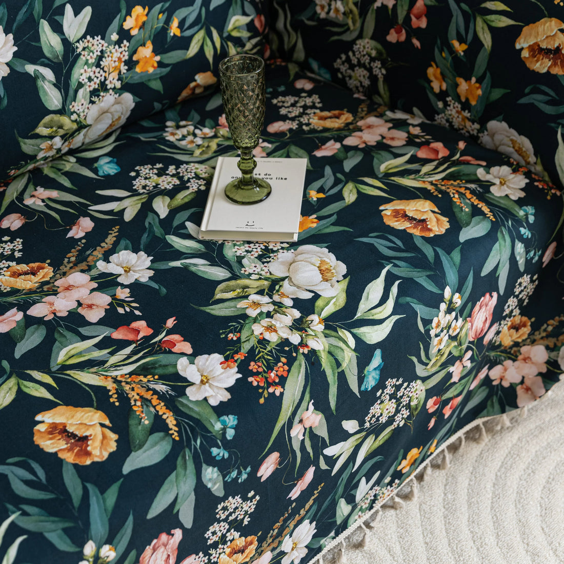Elegant floral sofa cover with a dark navy background, featuring vibrant blossoms and green foliage, accented with white tassel trim.