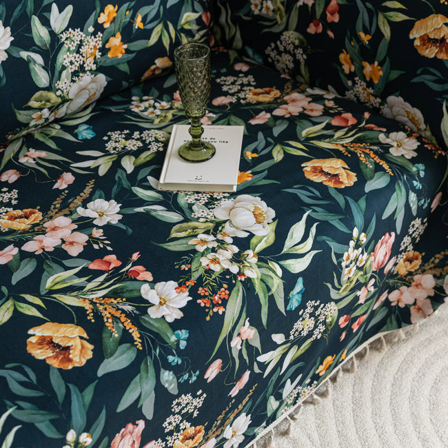 Elegant floral sofa cover with a dark navy background, featuring vibrant blossoms and green foliage, accented with white tassel trim.