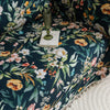 Elegant floral sofa cover with a dark navy background, featuring vibrant blossoms and green foliage, accented with white tassel trim.