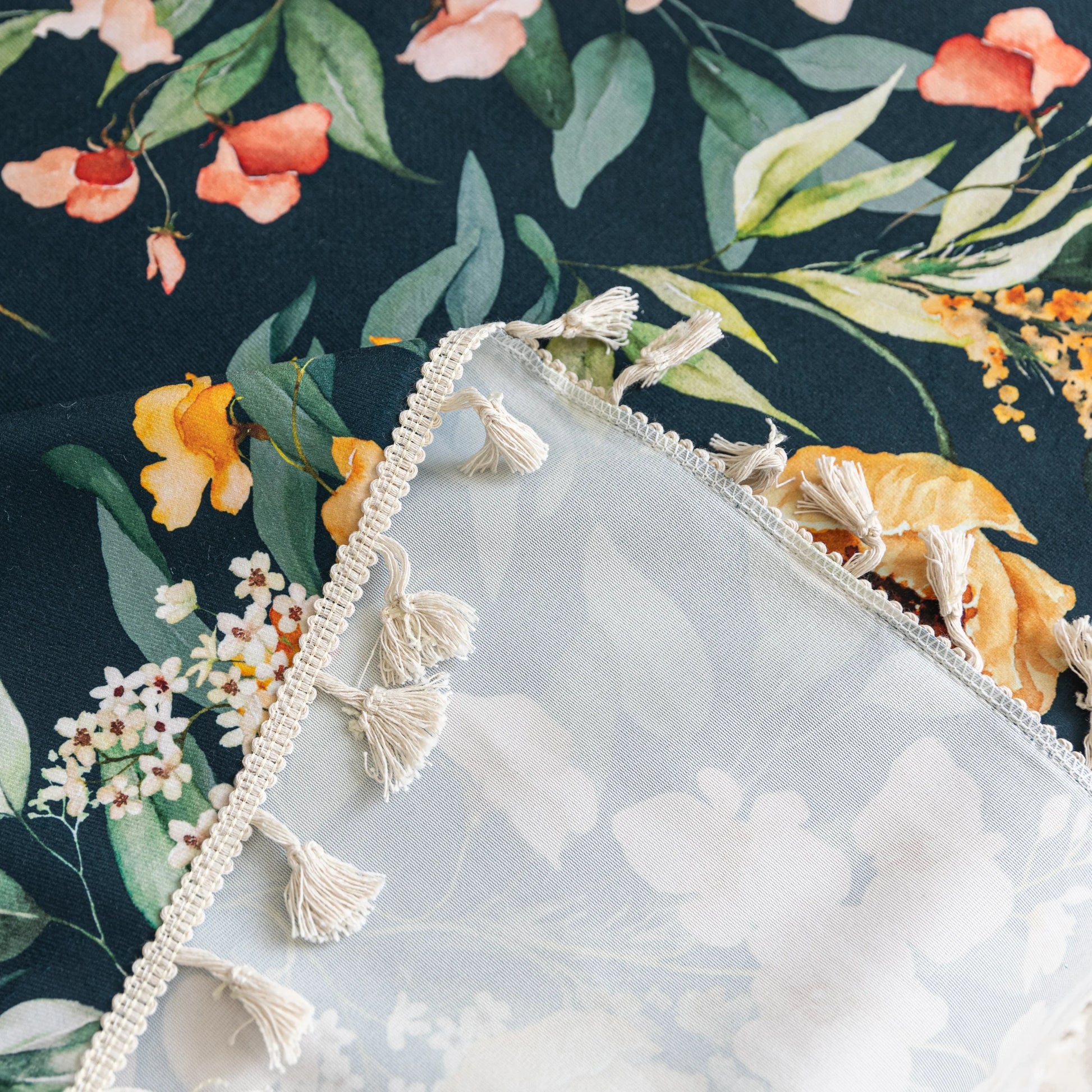 Elegant floral sofa cover with a dark navy background, featuring vibrant blossoms and green foliage, accented with white tassel trim.
