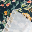 Elegant floral sofa cover with a dark navy background, featuring vibrant blossoms and green foliage, accented with white tassel trim.