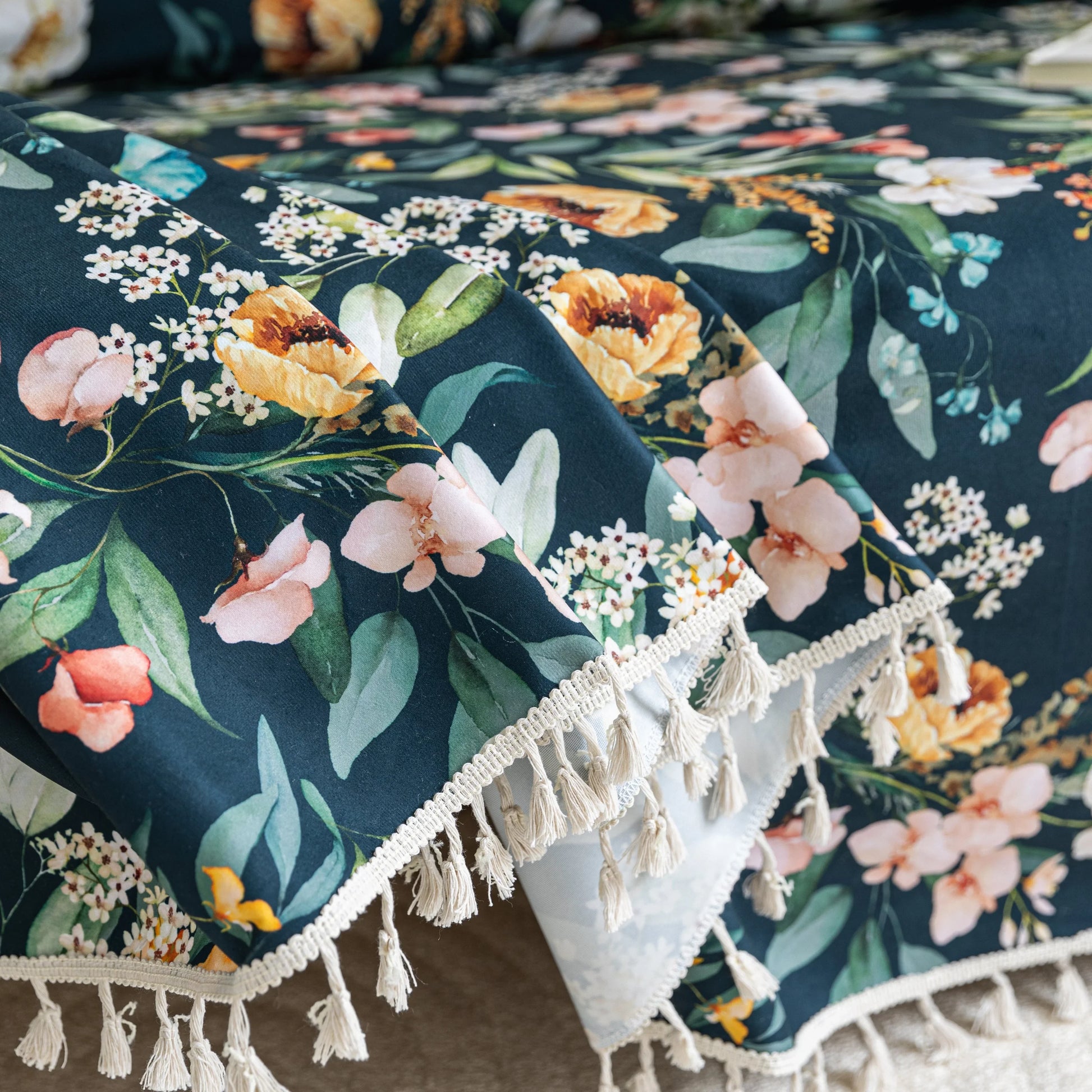 Elegant floral sofa cover with a dark navy background, featuring vibrant blossoms and green foliage, accented with white tassel trim.