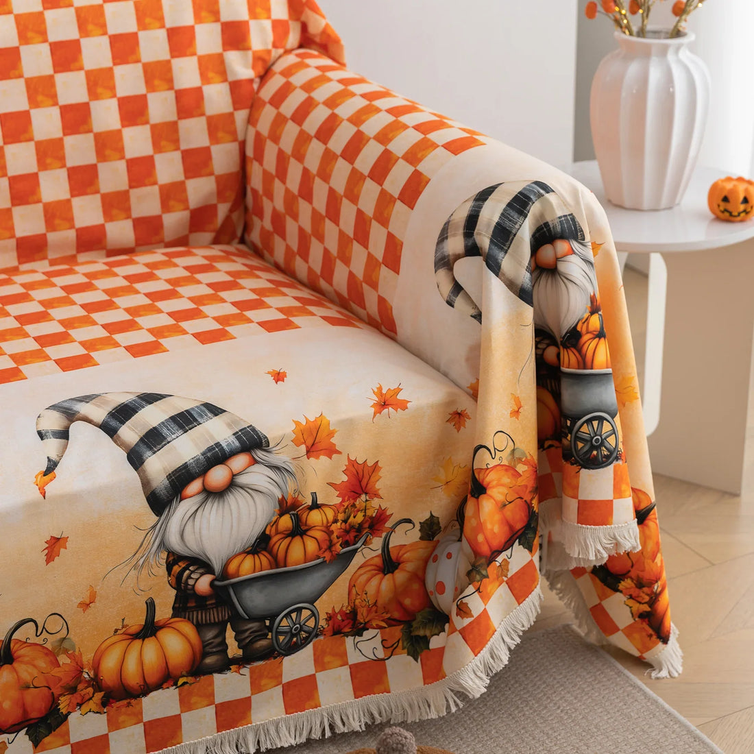 Autumn-themed sofa cover with an orange and white checkerboard pattern on the backrest and whimsical gnome illustrations on the seat, surrounded by pumpkins, leaves, and wheelbarrows, creating a cozy seasonal look.