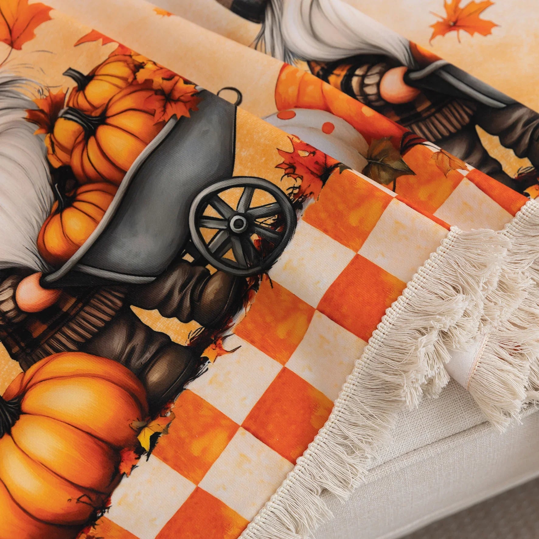 Autumn-themed sofa cover with an orange and white checkerboard pattern on the backrest and whimsical gnome illustrations on the seat, surrounded by pumpkins, leaves, and wheelbarrows, creating a cozy seasonal look.