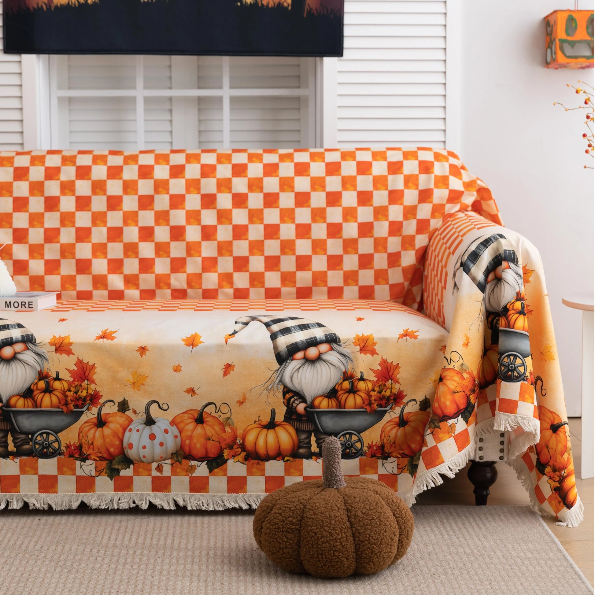 Autumn-themed sofa cover with an orange and white checkerboard pattern on the backrest and whimsical gnome illustrations on the seat, surrounded by pumpkins, leaves, and wheelbarrows, creating a cozy seasonal look.